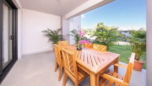 A balcony with a wooden table and chairs, potted plants, and a view of a beach and greenery. - The Pearl Jaco Beach (Jacó)