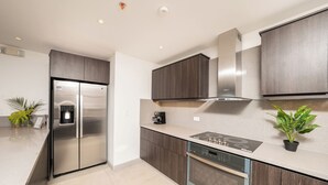 A modern kitchen with a stainless steel refrigerator, built-in oven, and a stove. - The Pearl Jaco Beach (Jacó)