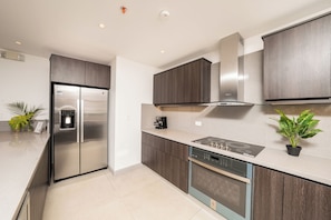 A modern kitchen with a stainless steel refrigerator, built-in oven, and a stove. - The Pearl Jaco Beach (Jacó)
