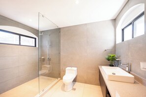 Een moderne badkamer met een douchecabine van glas, een toilet, een wastafel en een potplant.