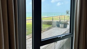 Una ventana con vista al océano, una terraza de madera y plantas en macetas.