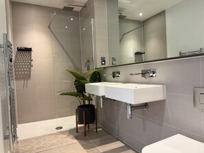 Ein modernes Badezimmer mit einer Duschkabine, zwei Waschbecken, einem großen Spiegel und einer Zimmerpflanze.