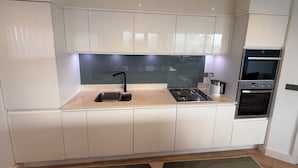 Una cocina moderna con armarios blancos, un lavamanos de acero inoxidable, una estufa a gas y un horno empotrado.