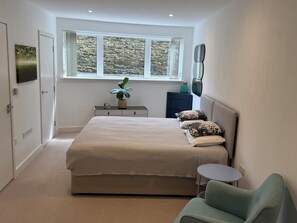 Ein Schlafzimmer mit Bett, Nachttisch, Stuhl, Fenster und einer Pflanze.