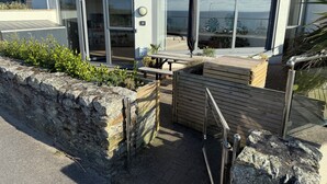 Un edificio moderno con un muro de contención de piedra, una terraza de madera y una barandilla de metal.
