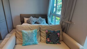 A beige sofa with two decorative pillows, one with a blue and white pattern and the other with a floral design, in a room with a window and curtains. - Room-city Condo Phuket Walk to Central (Wichit)