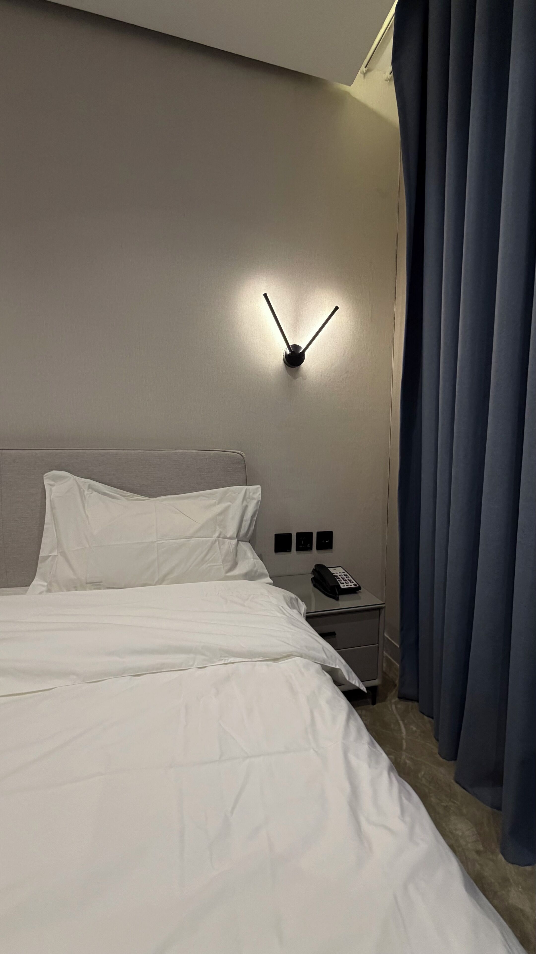 Habitación de hotel con una cama, una mesita de noche con teléfono y una lámpara de pared.