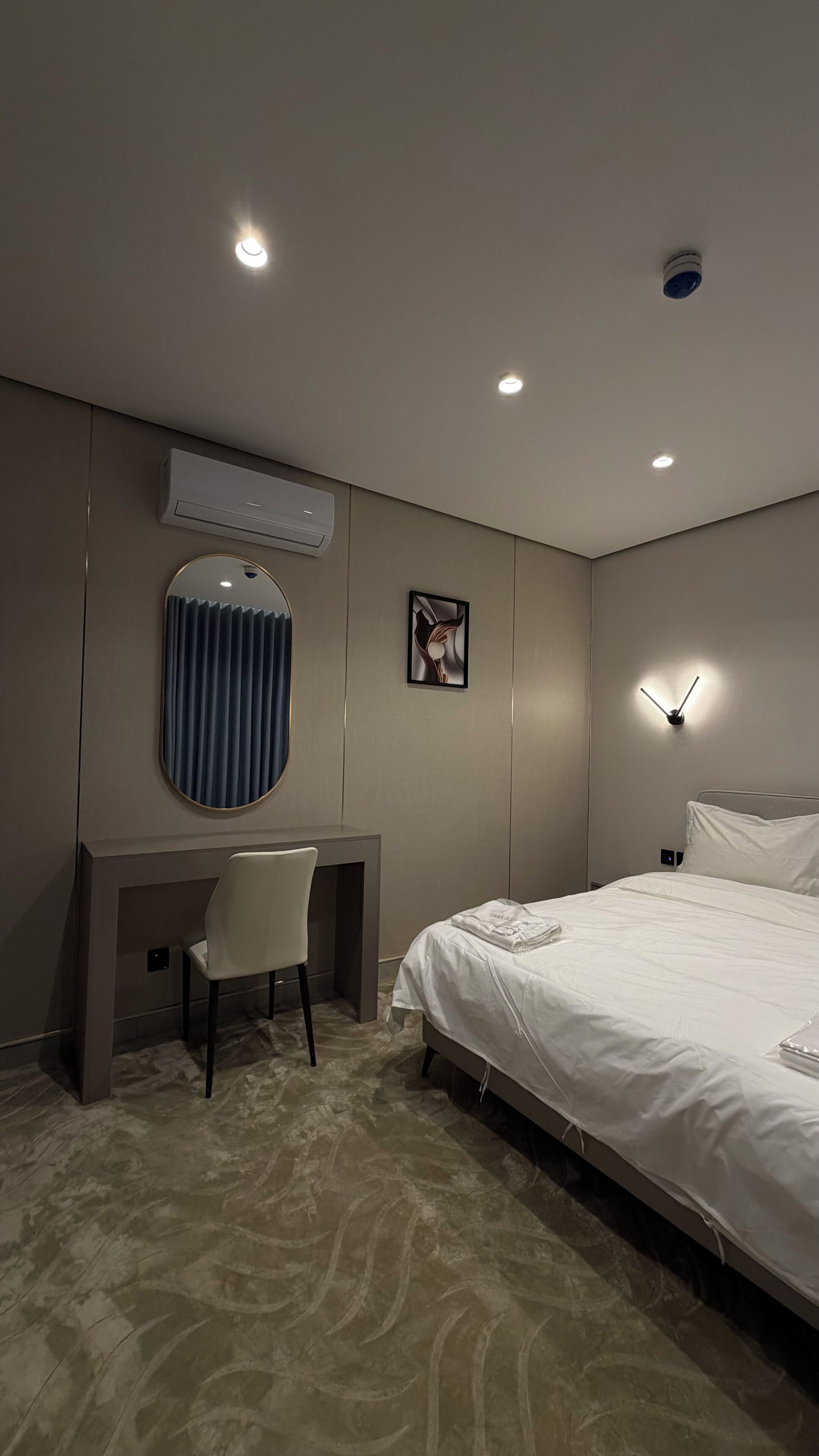 Habitación de hotel con cama, escritorio, silla, aire acondicionado de pared, un reloj y un cuadro en la pared.