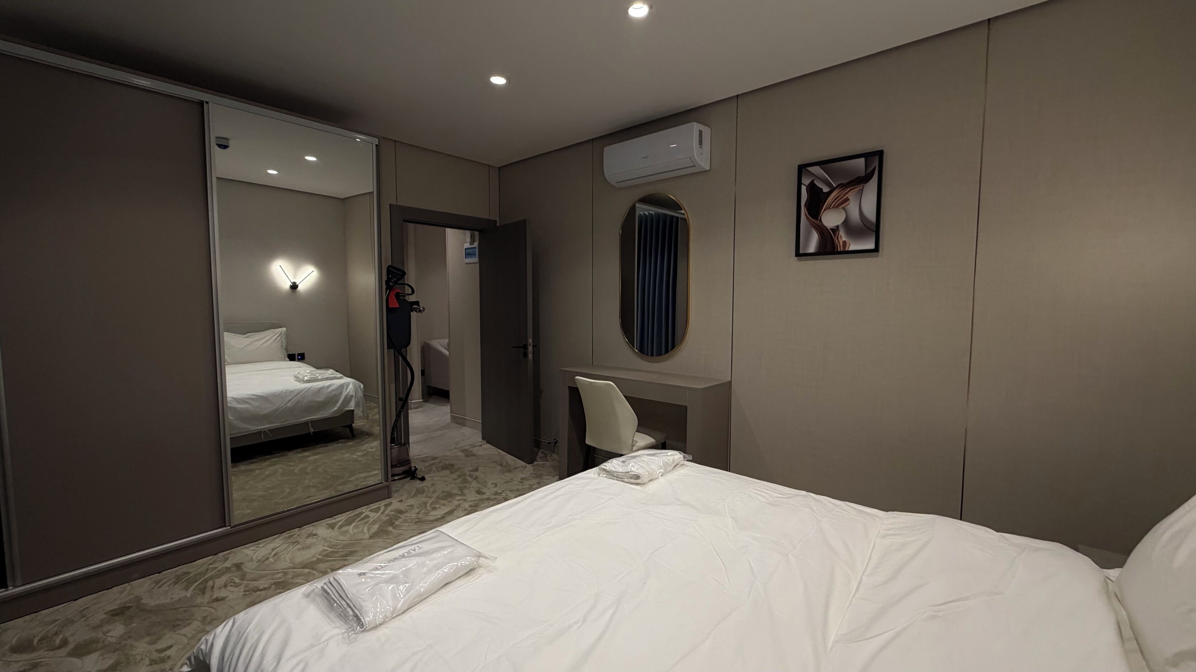 Camera d'albergo con un letto, una scrivania, una sedia, uno specchio, un condizionatore d'aria e un quadro appeso al muro.