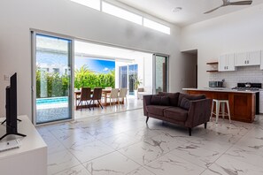 A modern living room with a sofa, a TV, and a kitchen area with cabinets and a countertop. - Private Sosua Villa, Pool, Bbq, Sosua Ocean Village (Sosúa)