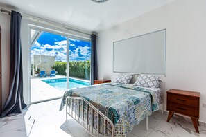 A bedroom with a bed, a bedside table, a nightstand, a large window, and a view of a swimming pool. - Private Sosua Villa, Pool, Bbq, Sosua Ocean Village (Sosúa)