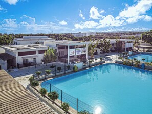 A swimming pool with a fenced area, a covered seating area, and buildings in the background. - Apartamentos en Parque Acuático (Sosúa)