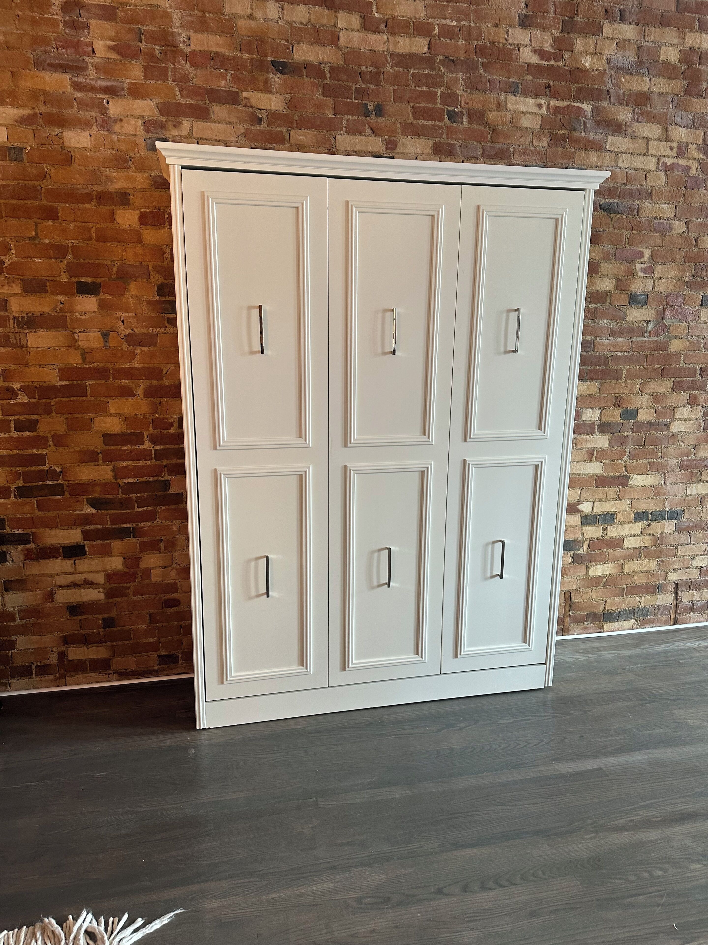 A white cabinet with six drawers against a brick wall.