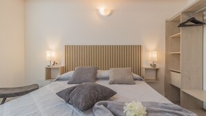 Ein Schlafzimmer mit einem Bett, Nachttischlampen, einem Kopfteil, einer Bank und einem Kleiderschrank.