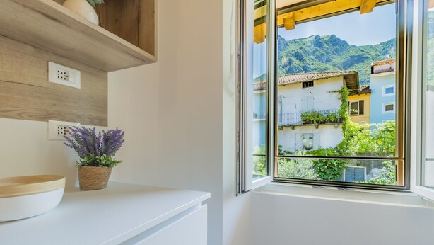 Eine Küche mit weißer Arbeitsplatte, einem Holzregal und einem Fenster mit Blick auf einen Berg und Gebäude.