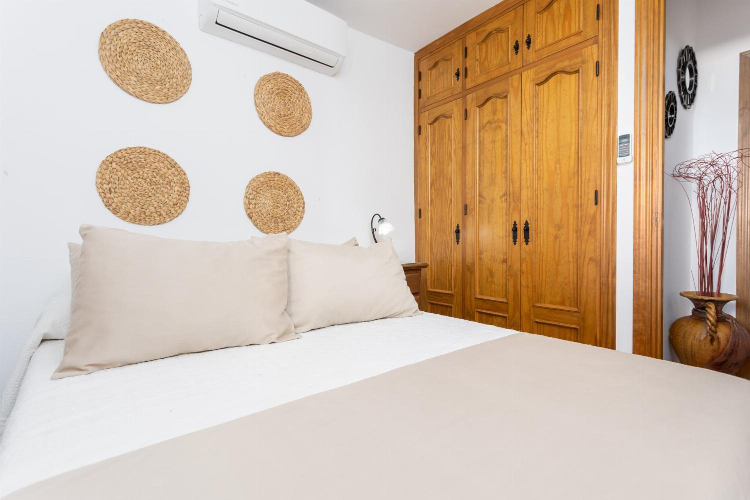 A bedroom with a bed, a wooden wardrobe, and woven wall decorations.