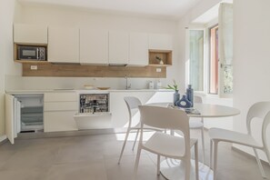 Eine moderne Küche mit weißen Schränken, einer eingebauten Mikrowelle und einem Essbereich mit weißen Stühlen und einem Tisch.