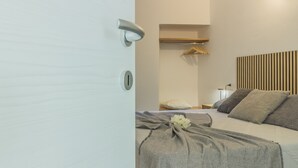 Un dormitorio con cama, mesita de noche, estante en la pared y una puerta.