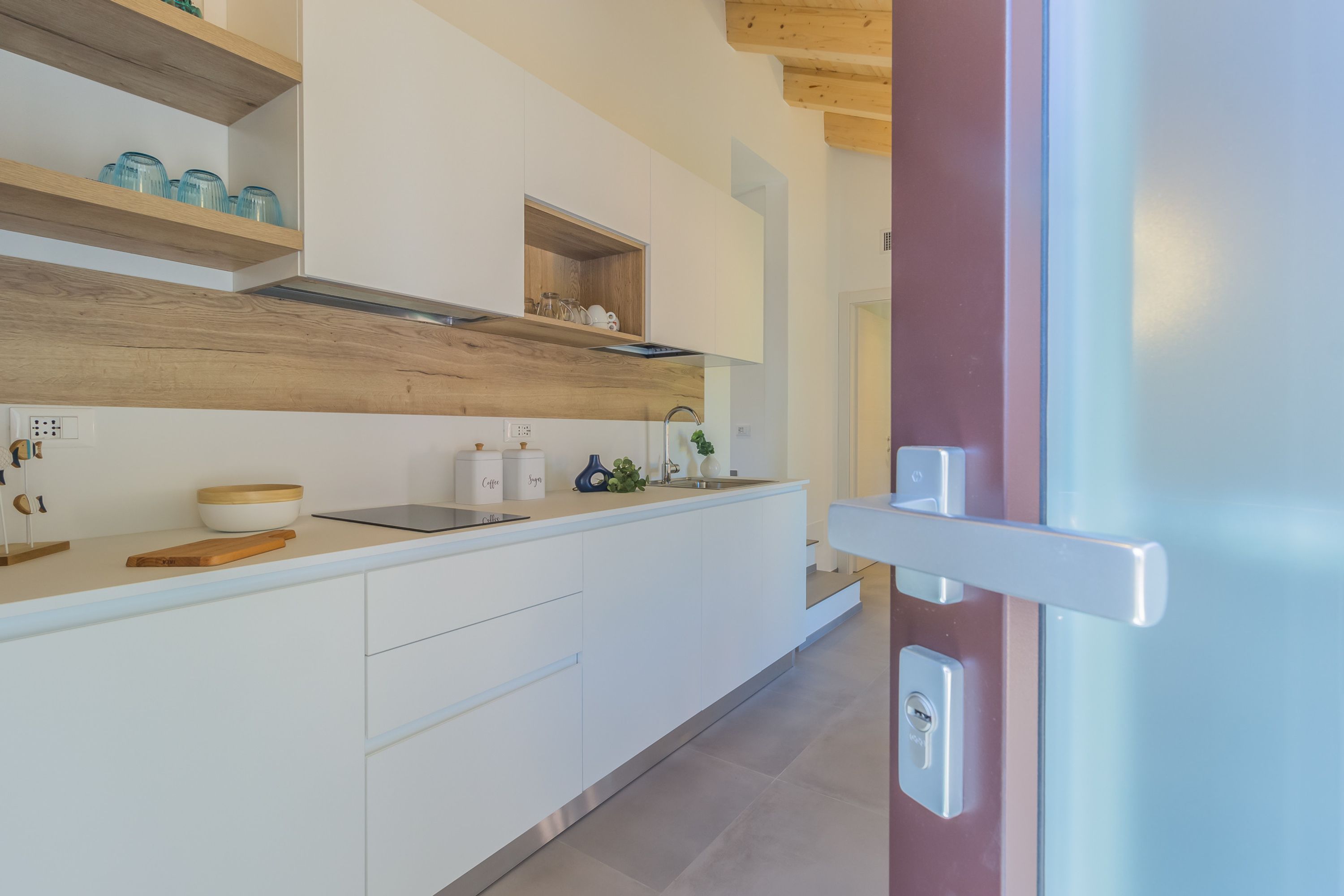 Una cocina moderna con armarios blancos, estantes de madera y horno empotrado.