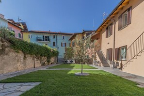 A courtyard with a small tree, a stone pathway, and colorful buildings with balconies. - C Magnolia Appartamento 4 (Lierna)