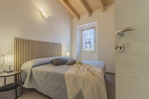 Un dormitorio con cama, mesitas de noche, lámpara, ventana y puerta.