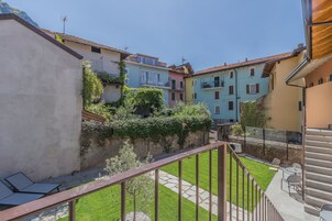 Una zona residencial con una escalera que lleva a un balcón, un pequeño jardín y edificios coloridos al fondo.