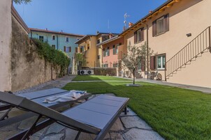 Un patio con césped, mobiliario exterior y una escalera que lleva a un edificio.
