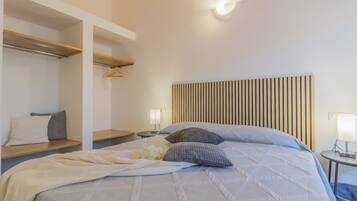 Un dormitorio con cama, mesitas de noche, estante colgante e iluminación en la pared.