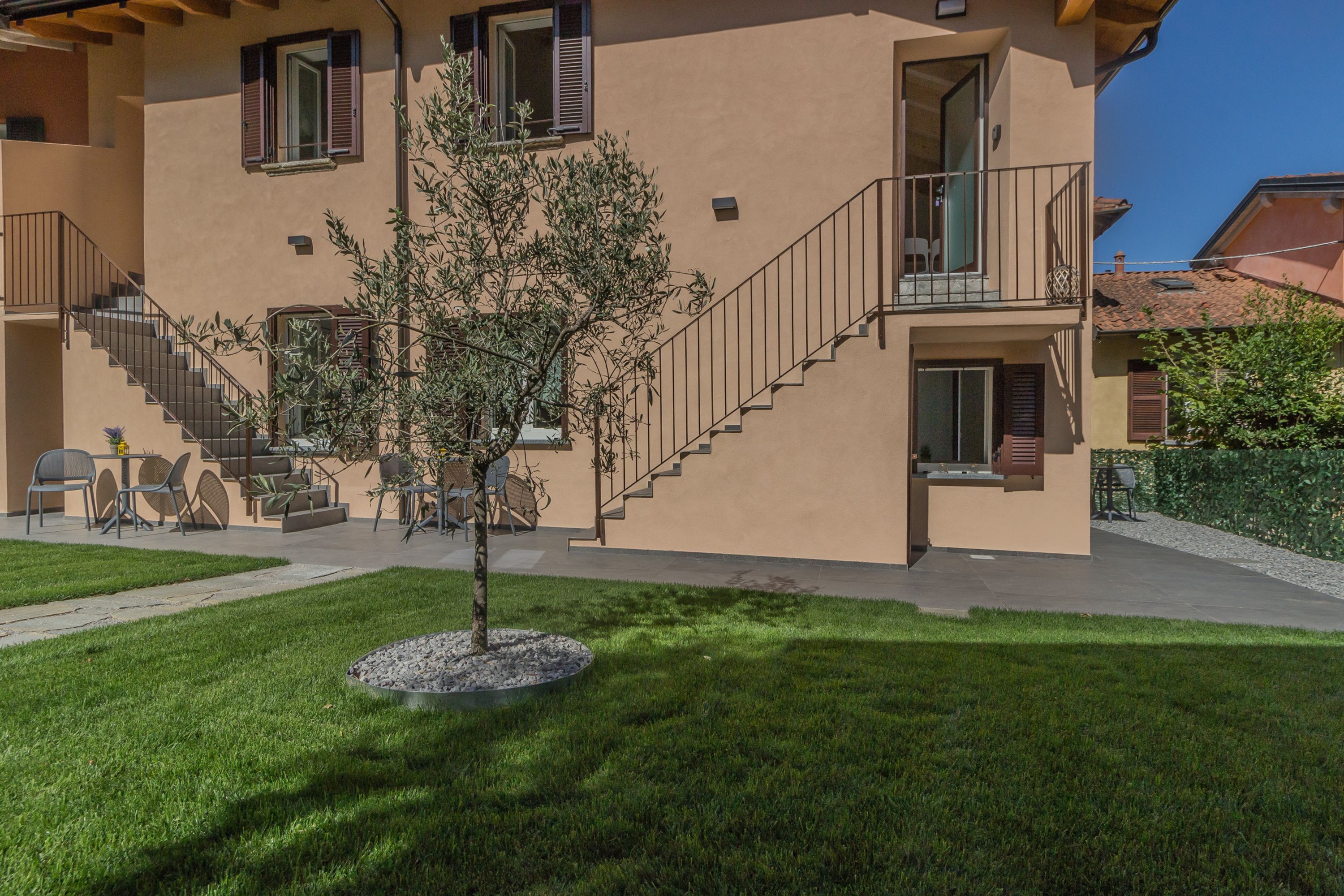 A two-story building with a staircase, outdoor seating, and a small tree in the front yard.