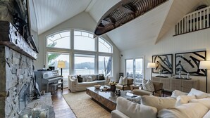 A spacious living room with a high ceiling, large windows, and a stone wall. - 6 bed 4 bath cottage on Lake Joseph (Port Carling)