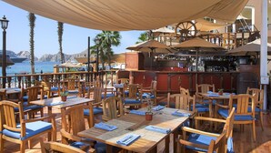 Ristorante all'aperto con tavoli e sedie in legno, zona bar e vista sul mare.