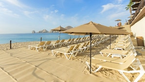 Un hotel sulla spiaggia con file di lettini e ombrelloni, vista libera sul mare e montagne sullo sfondo.