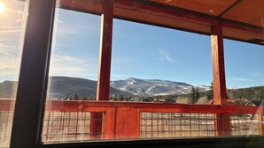 Blick durch ein Fenster mit Holzrahmen und Metallstreben auf eine verschneite Berglandschaft.