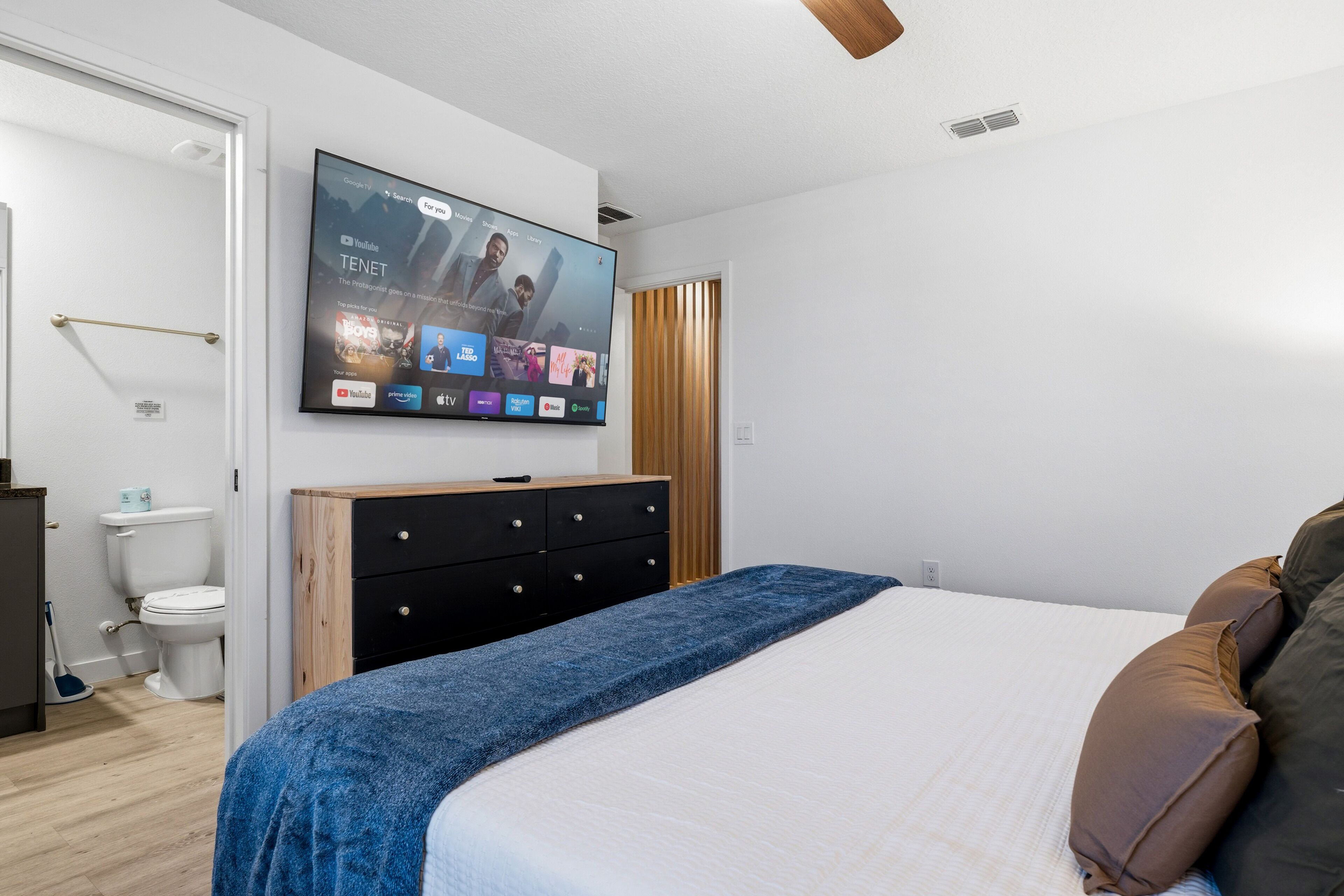 Ein modernes Schlafzimmer mit einem Bett, einem an der Wand montierten Fernseher, einer hölzernen Kommode und einer Toilette.