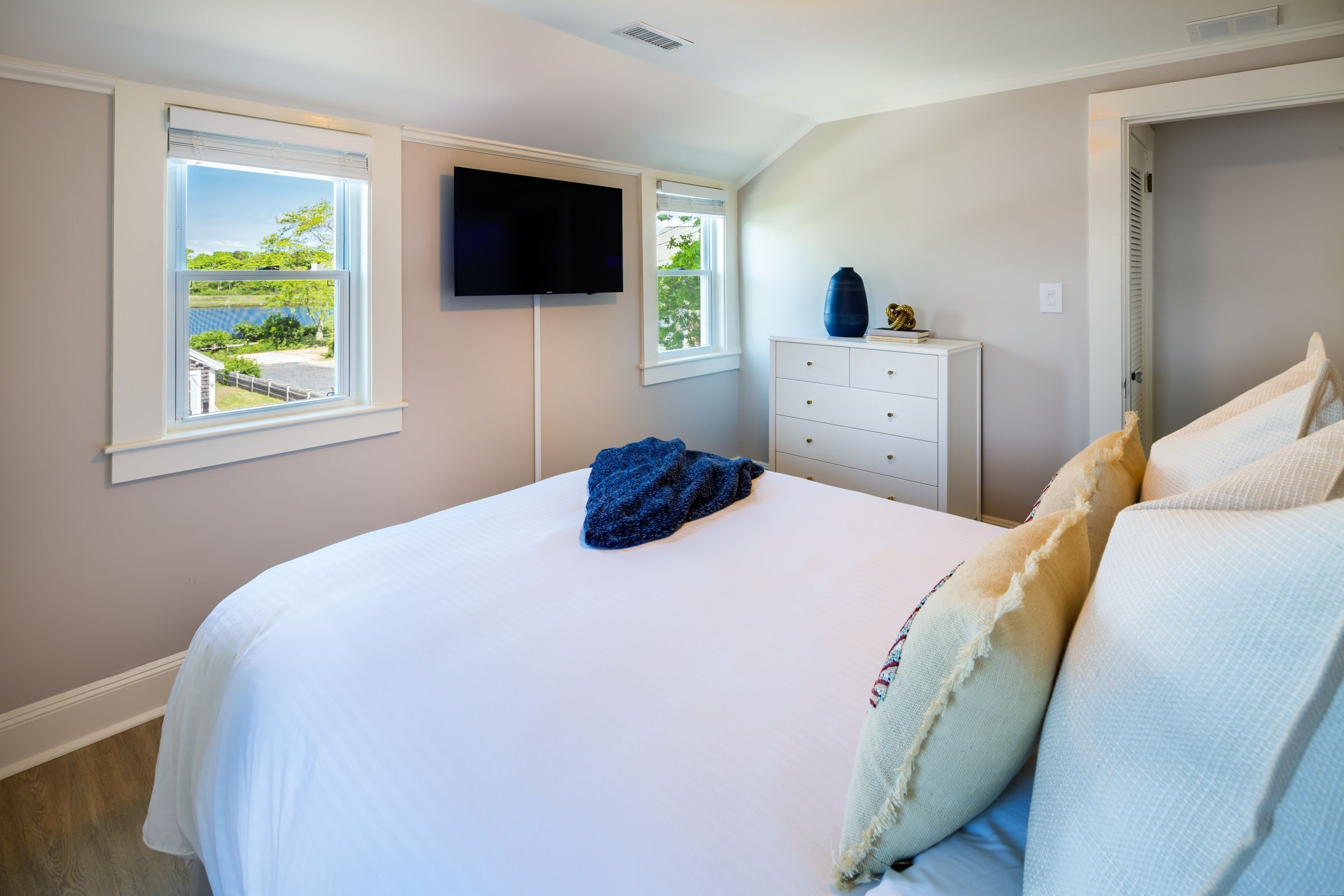 A bedroom with a bed, a dresser, a television, and a window with a view.