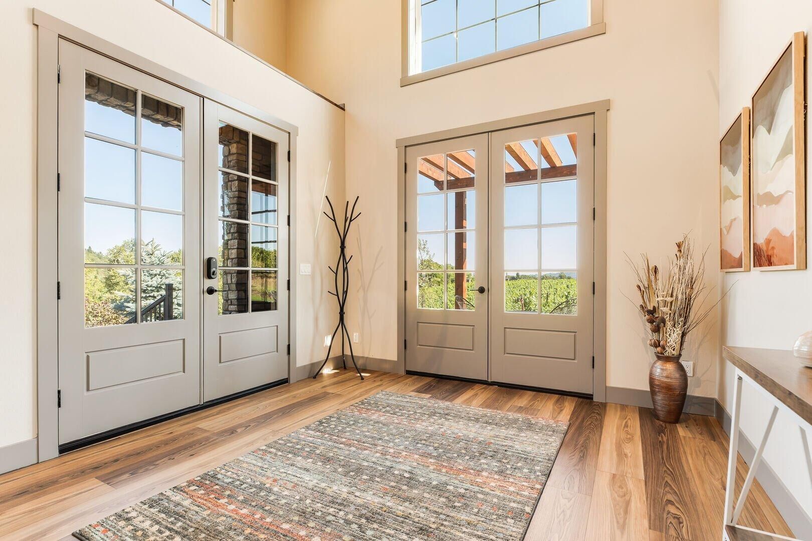 Un hall d’entrée spacieux, doté d’un plancher en bois, d’un tapis à motifs et offrant une vue sur un vignoble par les portes.