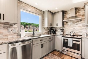 A modern kitchen with a large window, stainless steel appliances, and a stone backsplash.