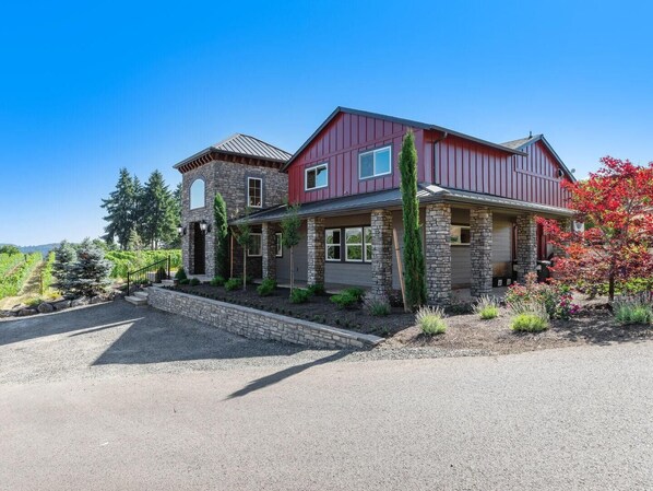 A two-story house with a stone facade, a red roof, and a driveway leading to a garage.