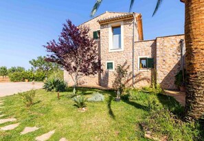 A stone building with a garden, a palm tree, and a clear sky.