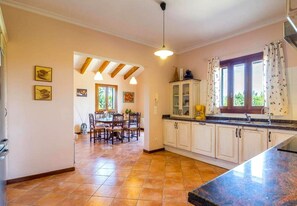A spacious kitchen with white cabinets, a dining area with wooden chairs, and a large window with curtains.
