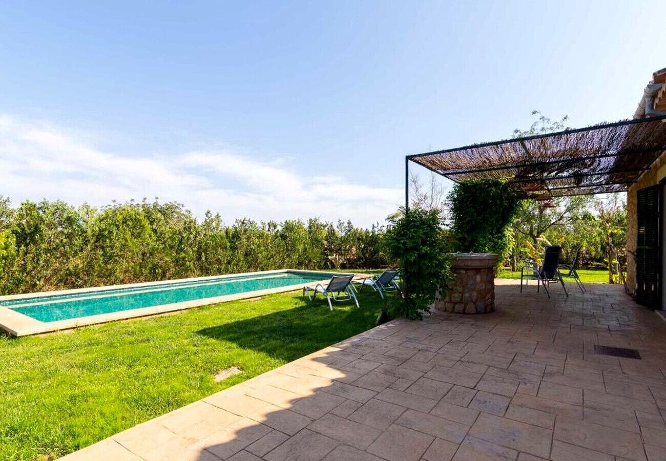 A backyard with a swimming pool, a patio with chairs, and a covered area.