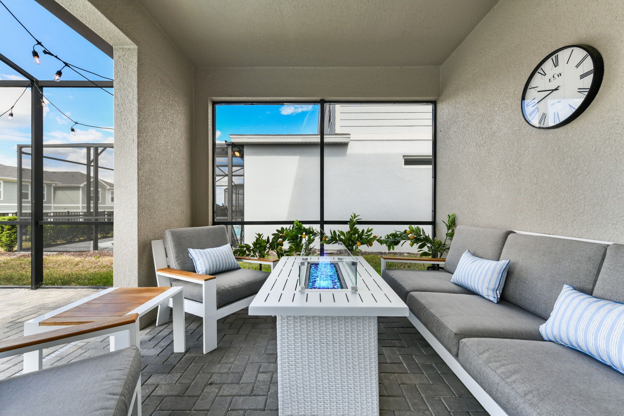 Un área de estar al aire libre moderna con una mesa blanca, un sofá gris y un reloj en la pared.