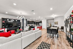 Ein modernes Wohnzimmer mit einem weißen Sofa, roten Kissen, einem Flachbildfernseher und einem Essbereich mit Tisch und Stühlen.