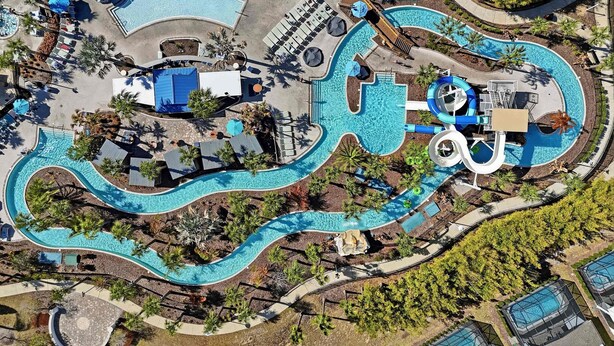 Luchtbeeld van een resort met meerdere zwembaden, ligbedden en palmbomen.