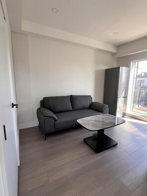Ein modernes Wohnzimmer mit grauem Sofa, einem мраморном журнальном столике und einem großen Fenster mit Tageslicht.