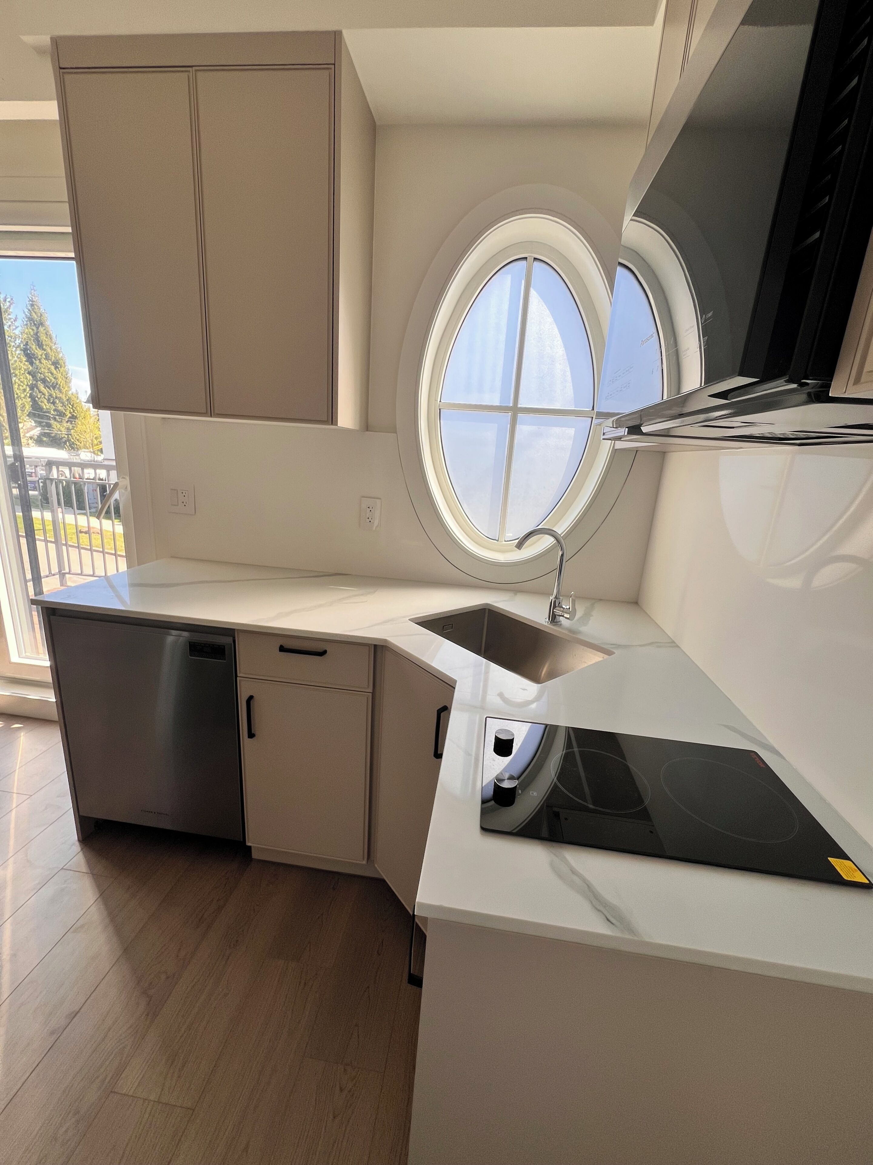 A modern kitchen with a built-in dishwasher, a window, and a black induction cooktop.