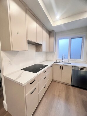 A modern kitchen with white cabinetry, a black induction cooktop, a stainless steel dishwasher, and a window with a view. - Big 3 bed+ 3 Bath townhome with rooftop views (Vancouver)