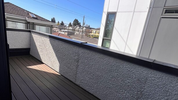A balcony with a wooden floor and a textured wall, overlooking a residential area with houses and a clear blue sky. - Modern Spacious 2 Bed 2 Bath Townhouse (Vancouver)