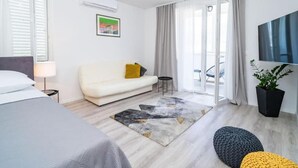 Una habitación de hotel moderna con cama, sofá, mesita, televisor y balcón con una silla.