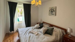 A bedroom with a bed, a chandelier, a painting, and a window with curtains. - Ston Heritage Apartment with City view (Ston)